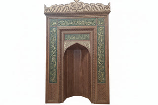 Decorative wooden archway with intricate carvings and calligraphy in a workshop setting.